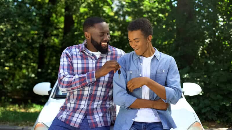 Happy dad giving car key to son with car insurance for teenagers