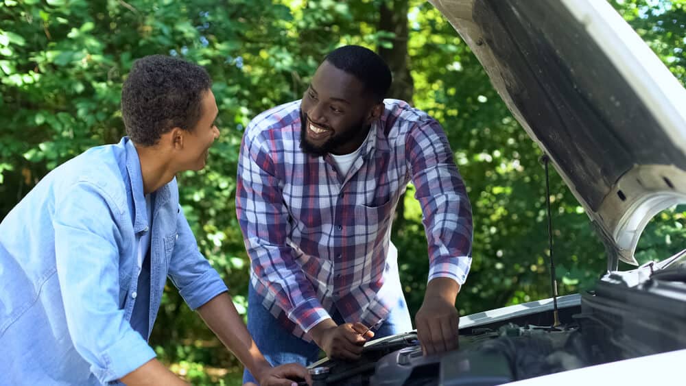 Father explaining car structure to son and smiling with car insurance for teenagers