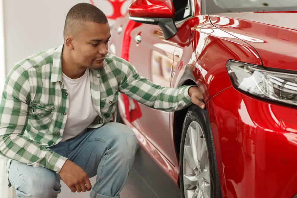 african american man checking tire pressure with no gauge on a red car