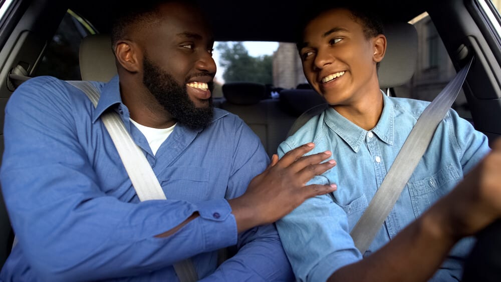 Smiling african american father praising teen son for driving well in alabama