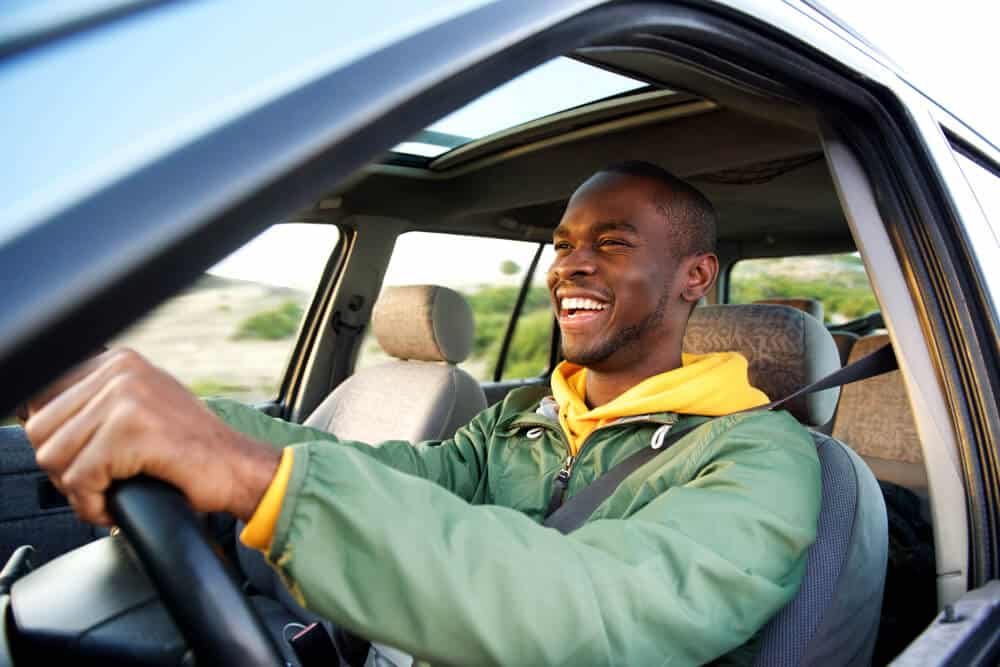 side view of african american young man driving car smiling