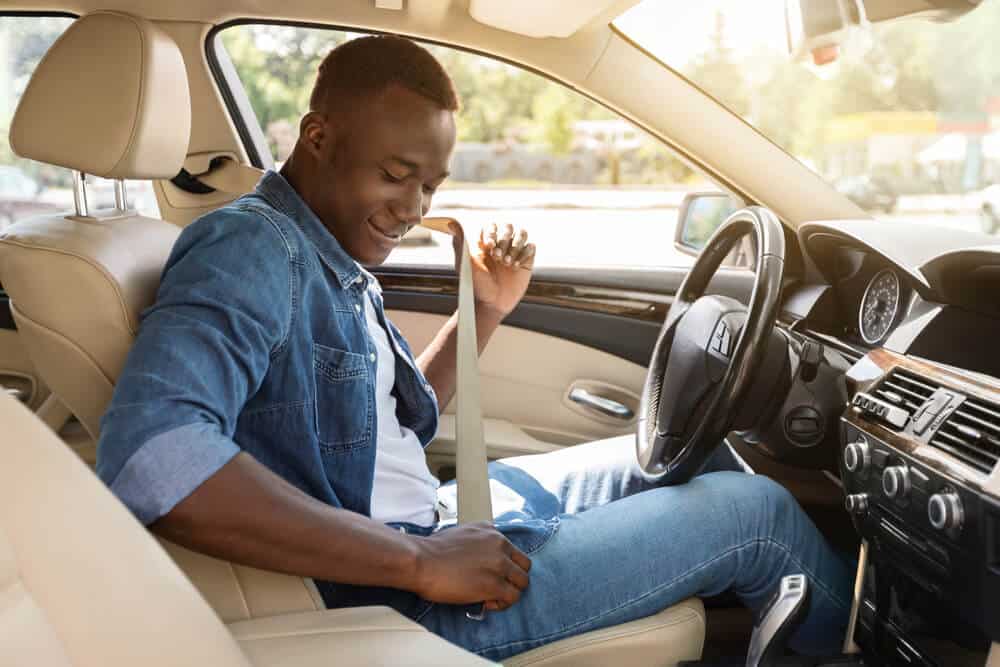 african american man in cars drivers seat putting on seatbelt
