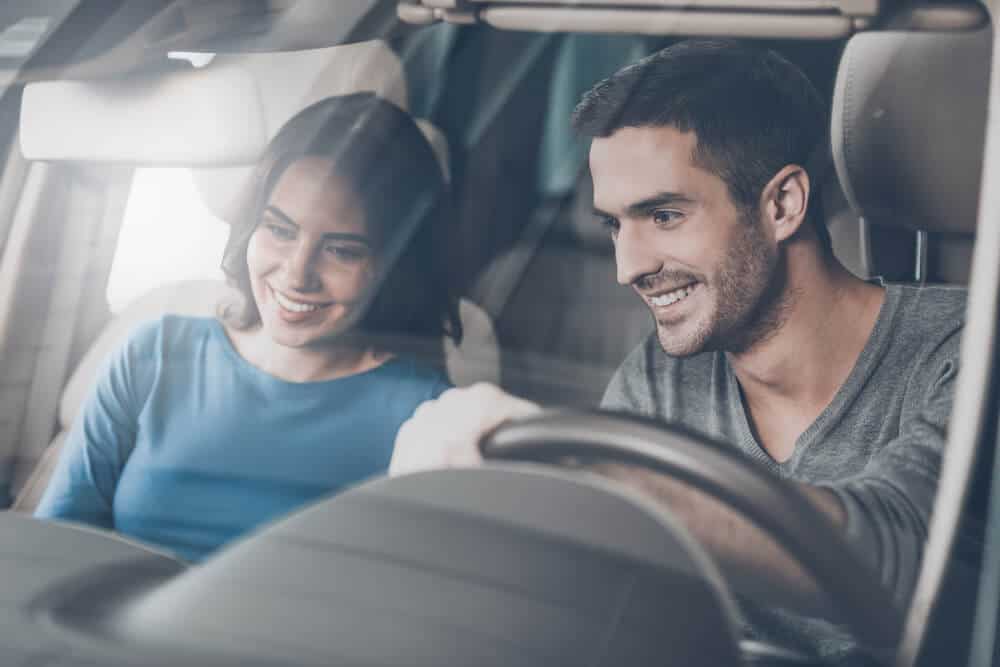young couple sitting at the front seat of the car checking out the side panel
