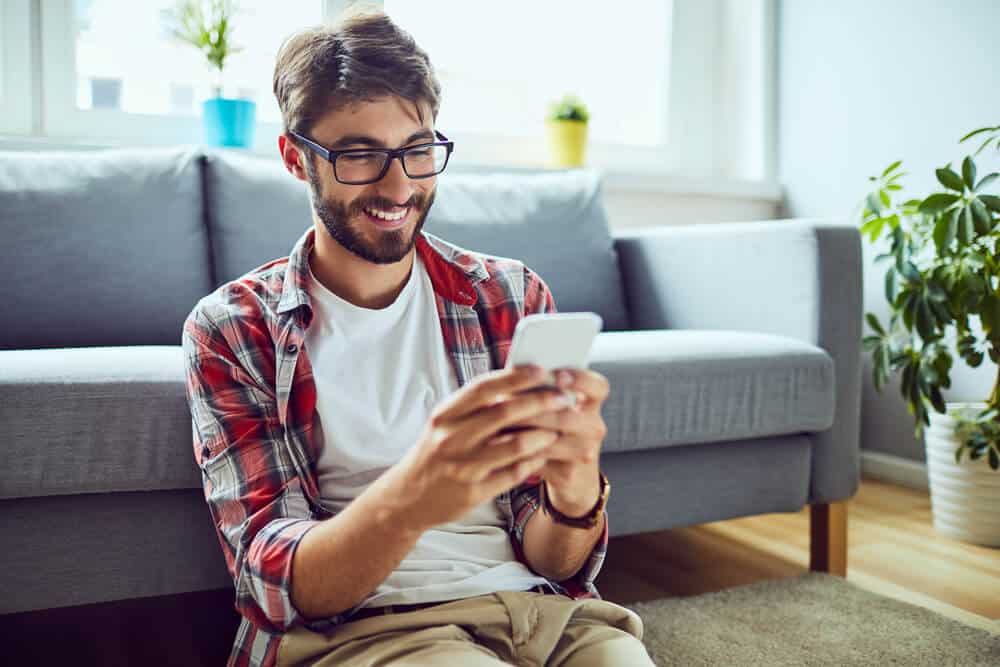 Smiling young man sitting on floor and looking for renters insurance