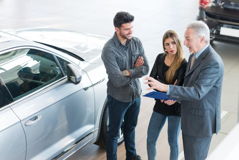 Happy,Young,Family,Talking,To,The,Salesman,And,Choosing,Their car salesman helping couple find a used car