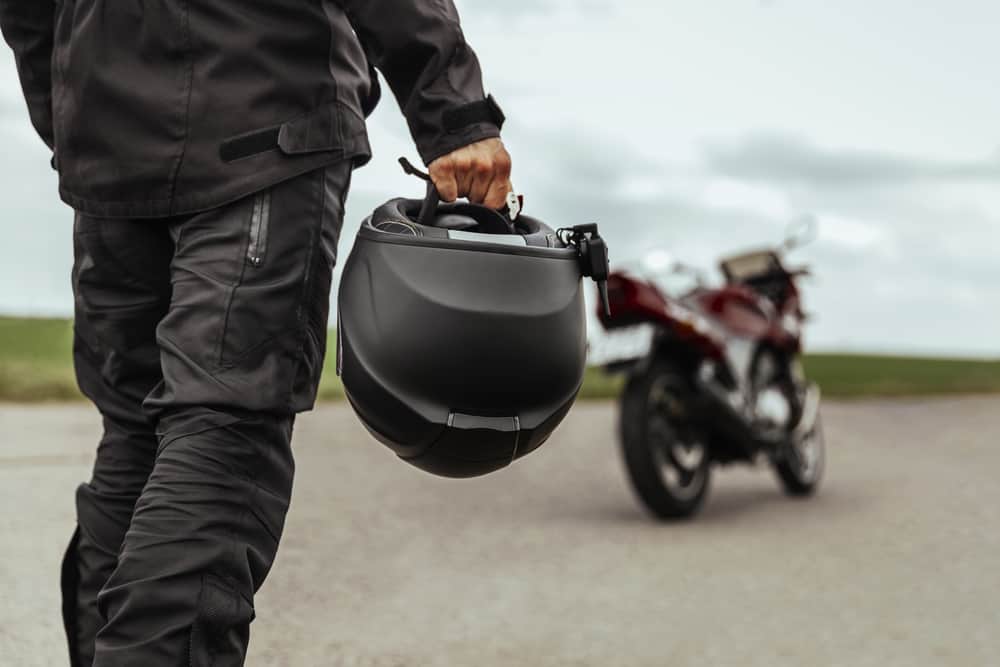 person walking towards motorcycle with helmet in hand