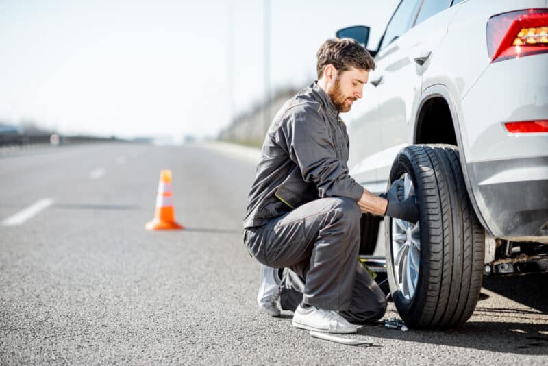 Handsome,Road,Assistance,Worker,In,Uniform,Changing,Car,Wheel,On young man helping change tire as part of roadside assistance help