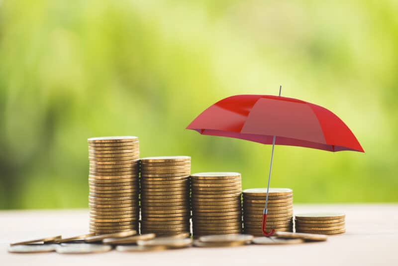 Red,Umbrella,Protects,Rows,Of,Increasing,Coins,On,Table.,Concept red umbrella over coins