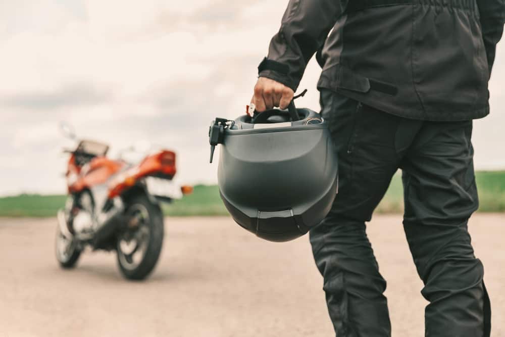 man walking to motorcycle with helmet in hand