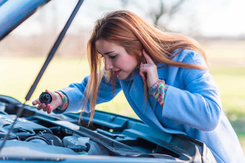 woman looking under hood of car on side of road