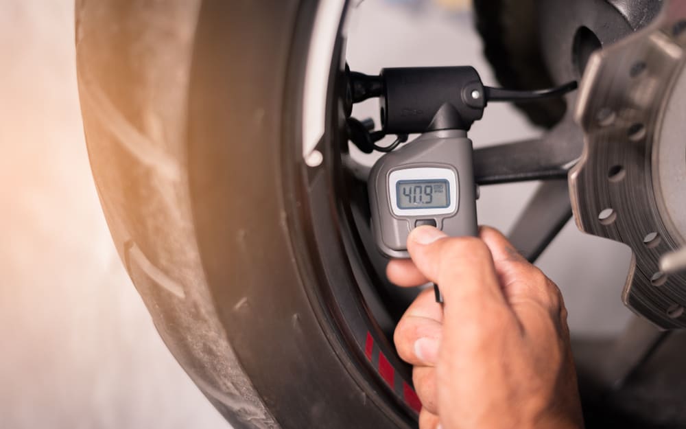 hand uses tire gauge to check pressure on motorcycle tire