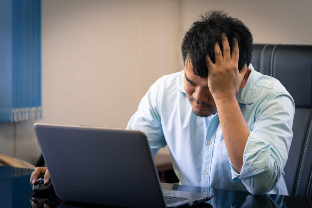 Worried young man sits in chair and looks at laptop