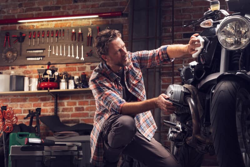 Low,Angle,Of,A,Man,Polishing,Classic,Vintage,Motorcycle,In man works on his motorcycle in his garage