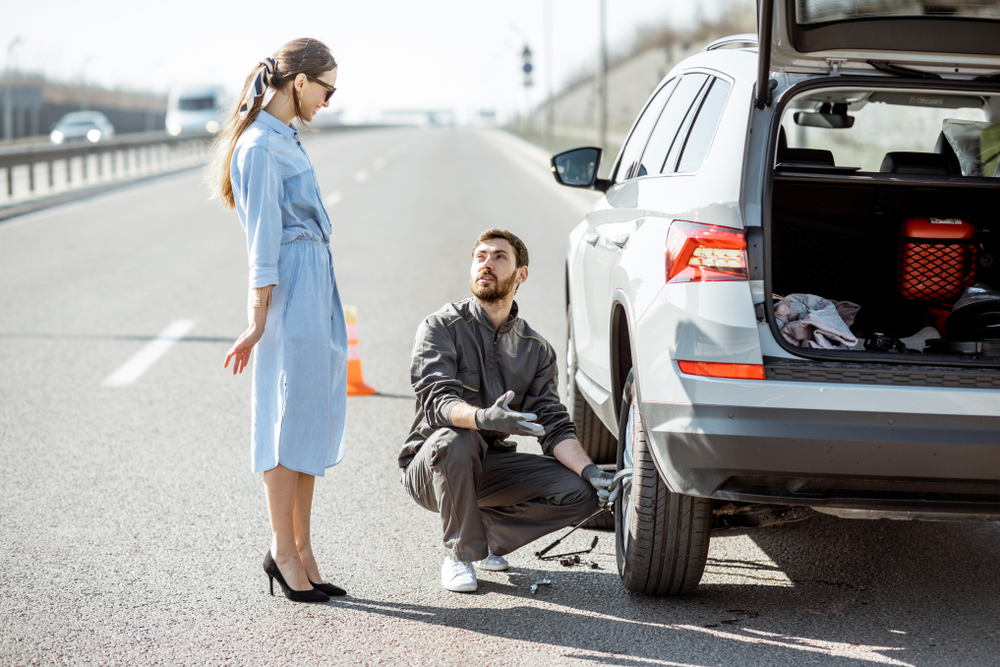 Woman watching as roadside assistance technician changes her tire