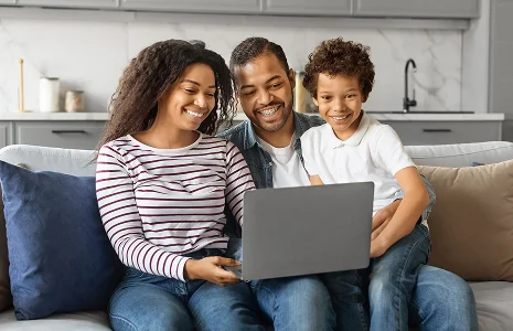 Happy family sitting on a couch, smiling and laughing together while looking at a laptop in their living room